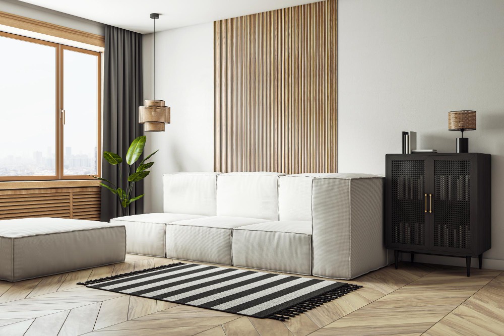 Современная светлая гостиная с акцентной стеной, облицованной вертикальными деревянными панелями, перед белым модульным диваном и черным шкафом в минималистичном стиле.